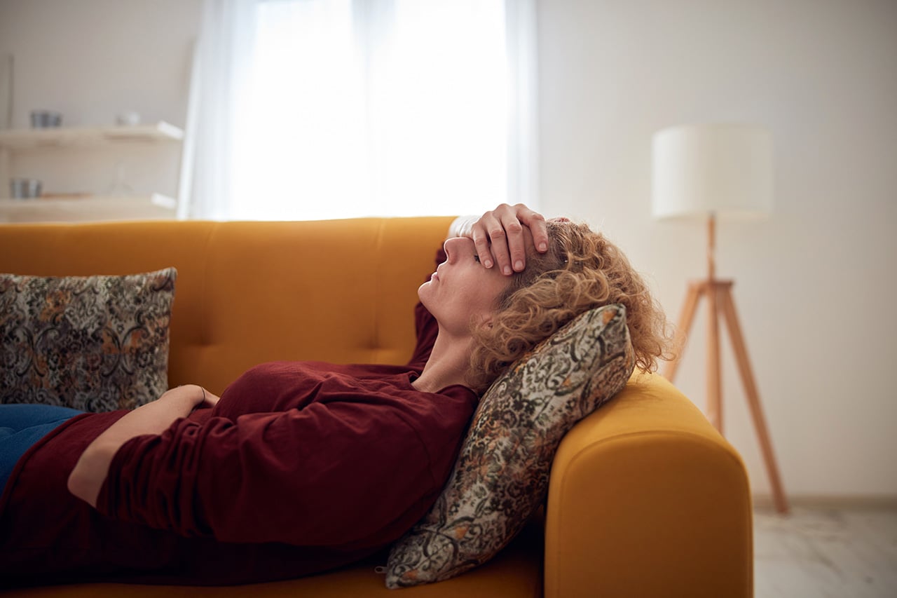 Kvinde ligger på sofa med hånden for panden som tegn på migræne akupunktur mod migræne som naturlig behandlingsform