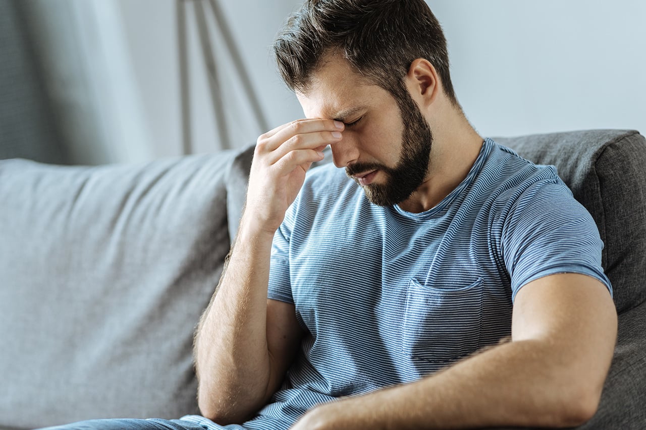 Mand sidder i sofa med symptomer på stress. Akupunktur kan hjælpe mod stress.